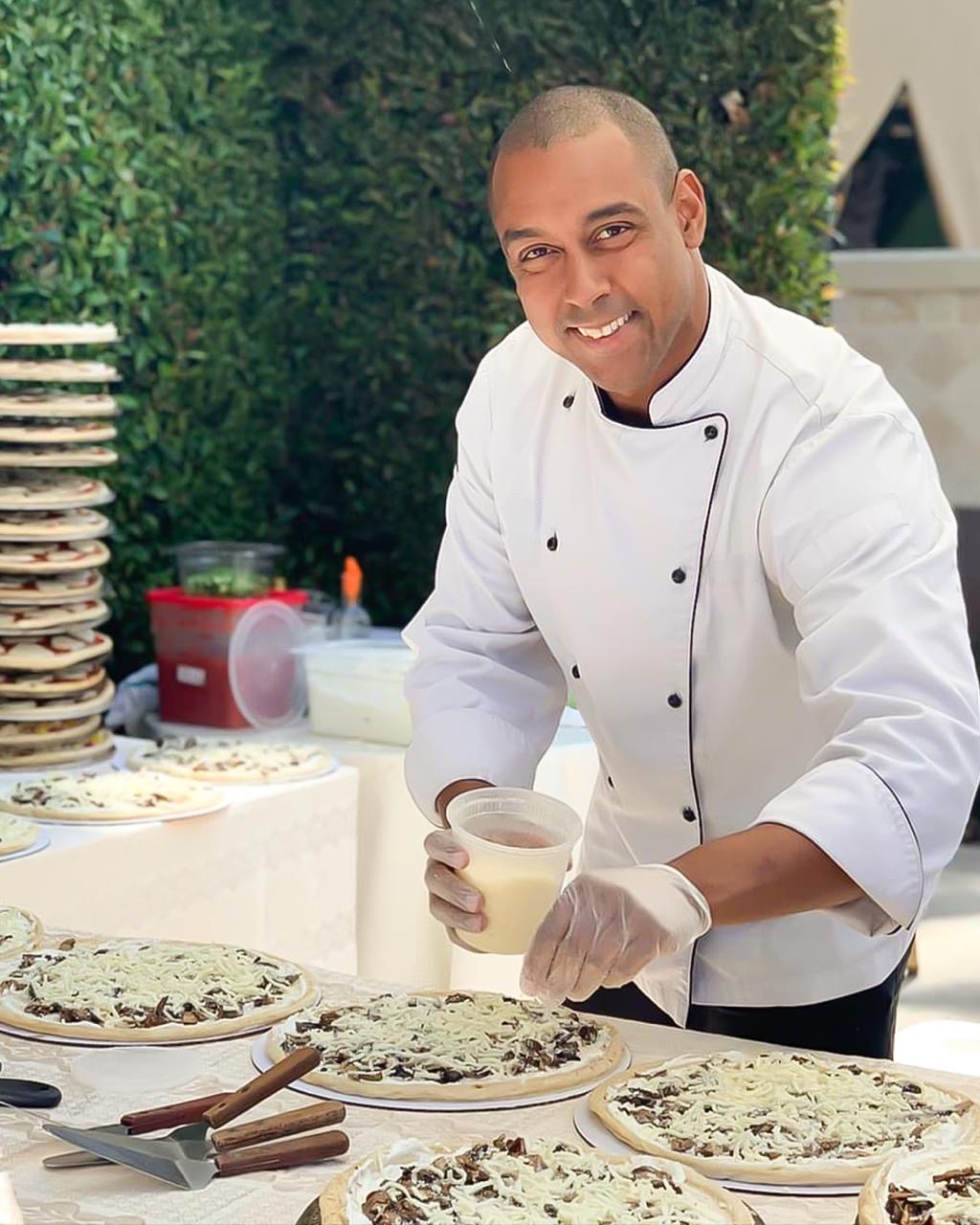 Smiling chef finishing fresh mushroom pizzas on a linen table at an Orange County catering event